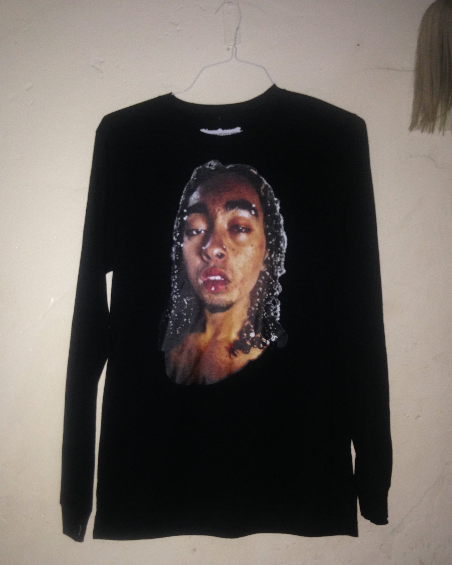 Black sleeveless shirt with a graphic of a face on a beige surface