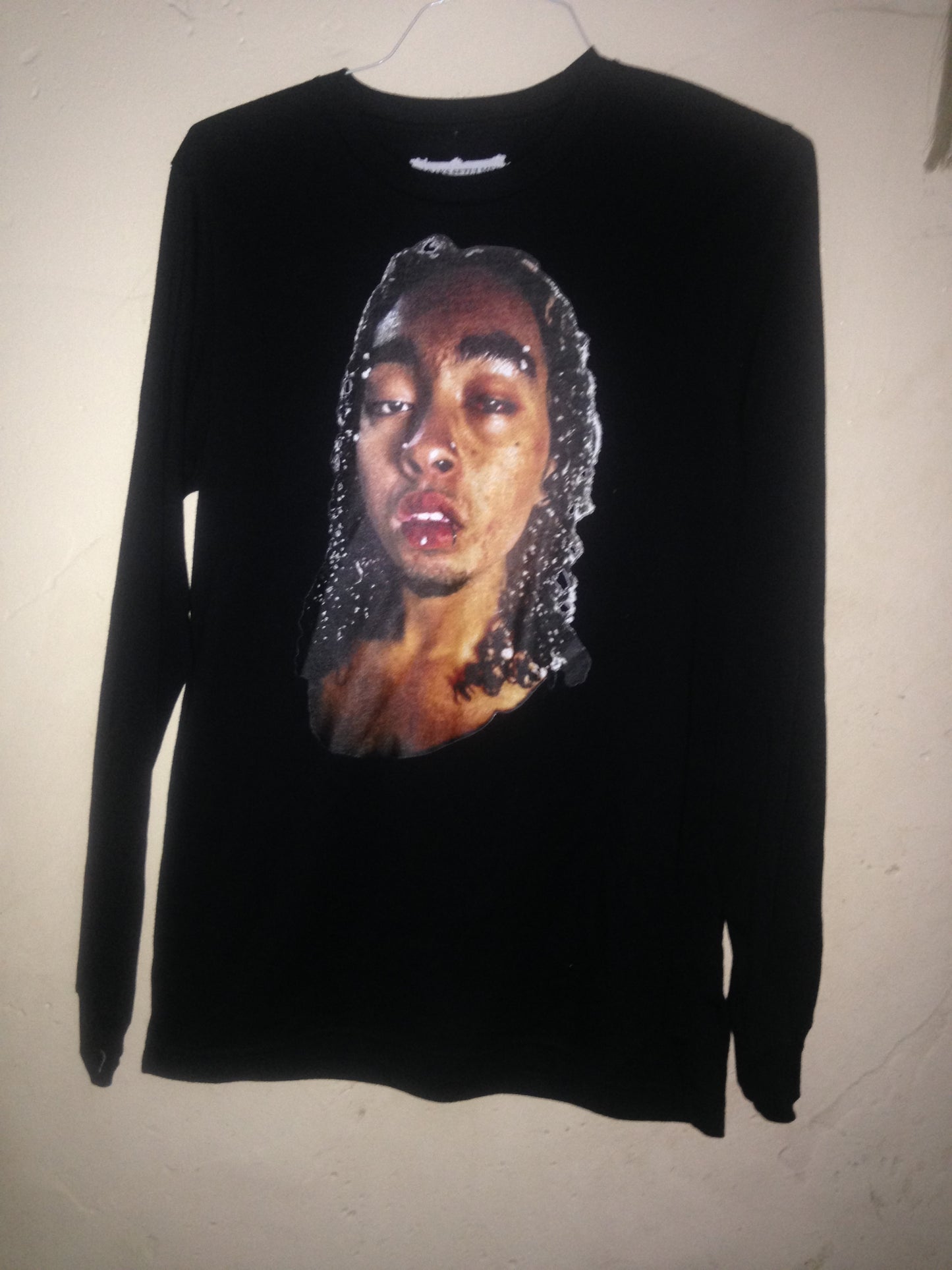 Black long-sleeve
 top with a graphic of a face on a beige background