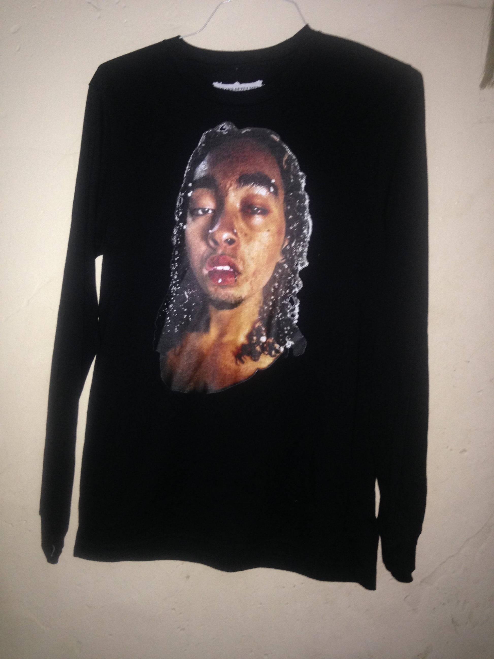 Black long-sleeve
 top with a graphic of a face on a beige background